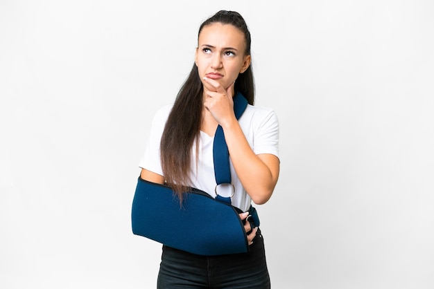 Young Arabian woman with broken arm and wearing a sling over isolated white background having doubts