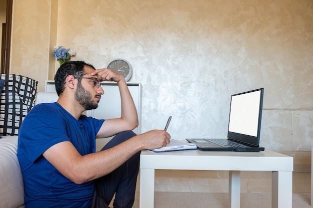 Young arabic man working at home with laptop and papers on desk