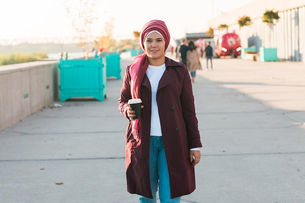Young arabic muslim woman in hijab walking at street seafront and drinking coffee take away copy spa