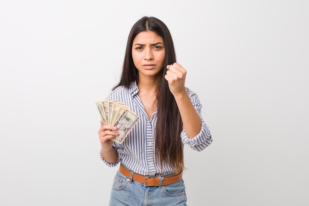 Young arabic  woman holding dollars showing fist to with aggressive facial expression.