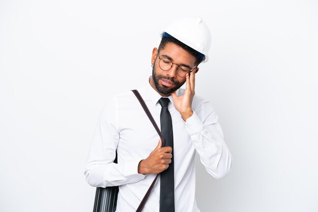 Young architect Brazilian man with helmet and holding blueprints isolated on white background with headache