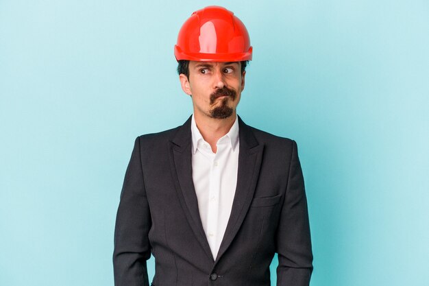 Young architect caucasian man isolated on blue background confused, feels doubtful and unsure.