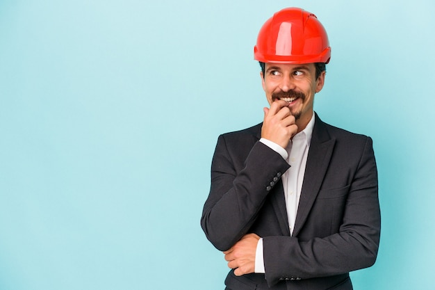 Young architect caucasian man isolated on blue background relaxed thinking about something looking at a copy space.