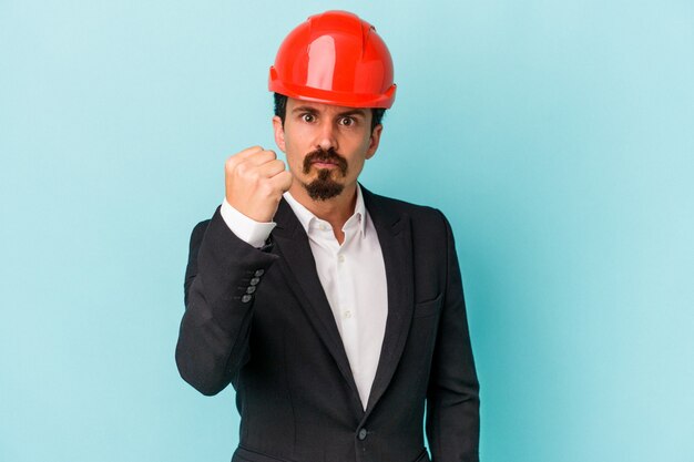 Young architect caucasian man isolated on blue background showing fist to camera, aggressive facial expression.