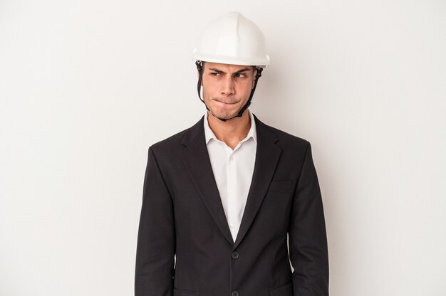 Young architect caucasian man isolated on white background confused, feels doubtful and unsure.