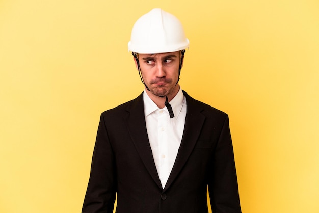 Young architect caucasian man isolated on yellow background confused, feels doubtful and unsure.