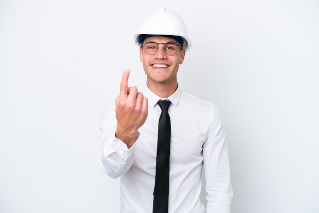 Young architect caucasian man with helmet and holding blueprints isolated on white background doing coming gesture