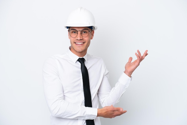 Young architect caucasian man with helmet and holding blueprints isolated on white background extending hands to the side for inviting to come