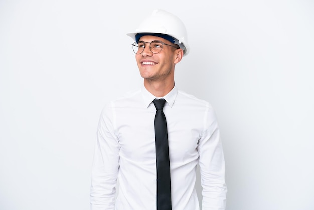 Young architect caucasian man with helmet and holding blueprints isolated on white background thinking an idea while looking up