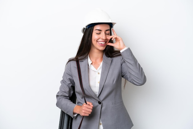 Young architect caucasian woman with helmet and holding blueprints isolated on white background laughing