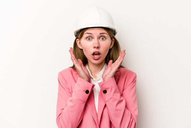 Молодой архитектор англичанка в шлеме на белом фоне удивлена и шокирована
