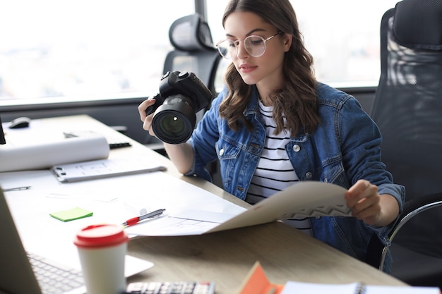 写真 クリエイティブオフィスで働いている間、デジタルカメラを持って青写真を見ている若い建築家。