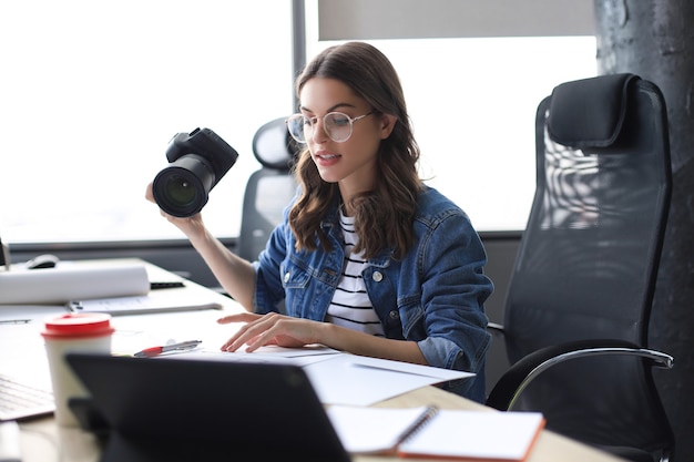 Young architect holding digital camera and looking on blueprint while working in the creative office.