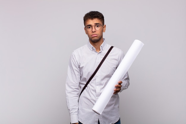 Young architect man feeling sad and whiney with an unhappy look, crying with a negative and frustrated attitude