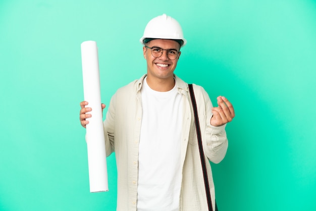 Young architect man holding blueprints over isolated background making money gesture