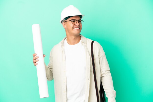 Young architect man holding blueprints over isolated background thinking an idea while looking up