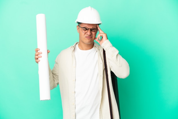 Young architect man holding blueprints over isolated background with headache