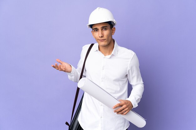 Young architect man isolated on wall having doubts while raising hands