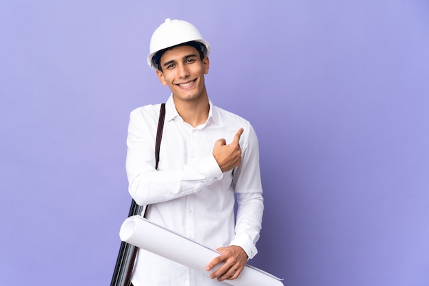 Young architect man isolated on wall pointing back