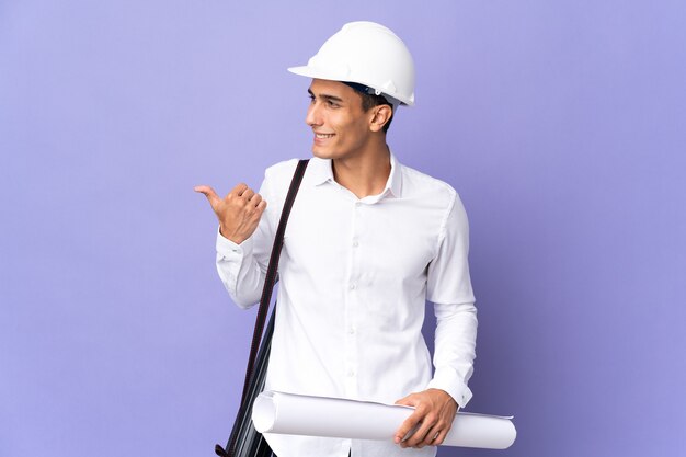 Young architect man isolated on wall pointing to the side to present a product