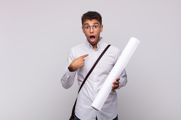 Young architect man looking shocked and surprised with mouth wide open, pointing to self