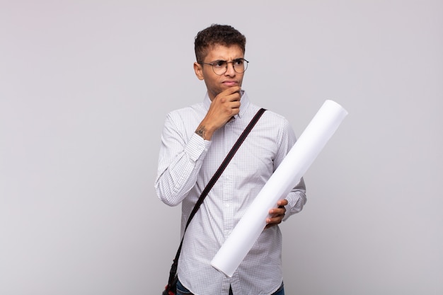 Young architect man thinking, feeling doubtful and confused, with different options, wondering which decision to make