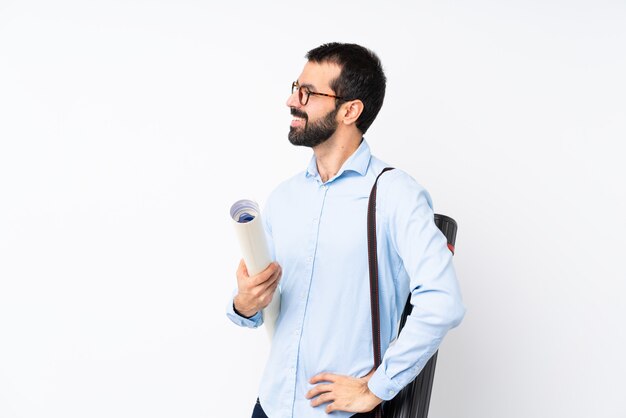 Giovane uomo dell'architetto con la barba sopra la parete bianca isolata che osserva al lato