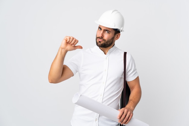 Young architect man with helmet and holding blueprints isolated on white proud and self-satisfied