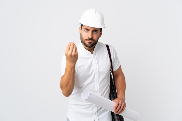 Young architect man with helmet and holding blueprints isolated on white wall making Italian gesture