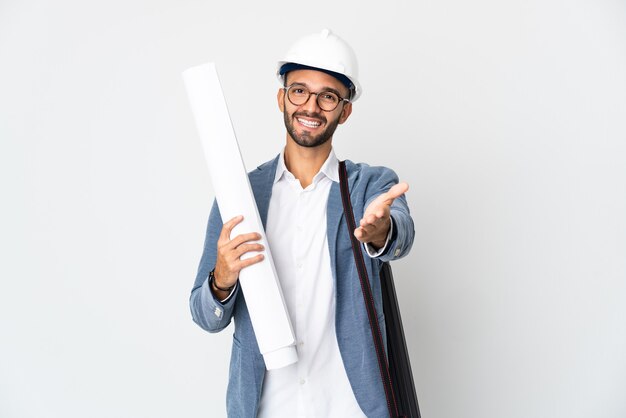 Young architect man with helmet and holding blueprints isolated on white wall shaking hands for closing a good deal