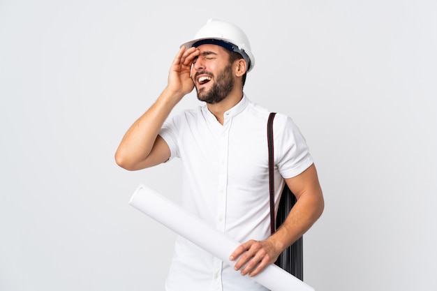 Young architect man with helmet and holding blueprints isolated on white wall smiling a lot