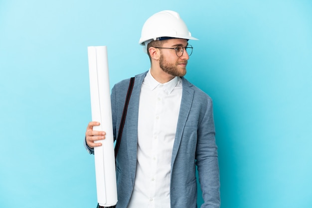 Young architect man with helmet and holding blueprints looking to the side