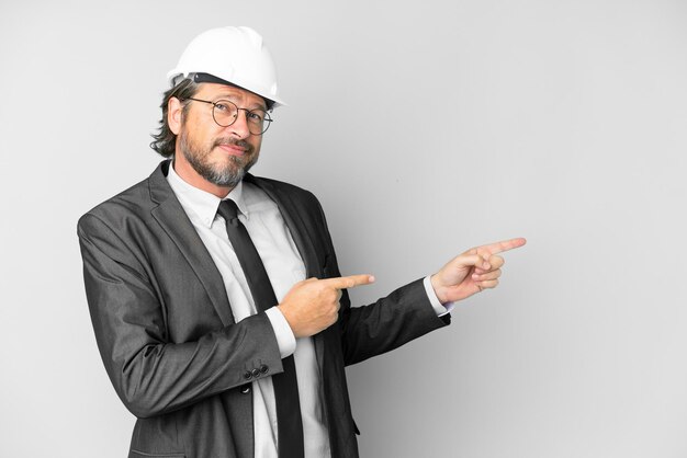 Young architect man with helmet over isolated background pointing finger to the side