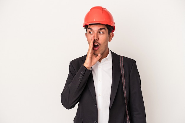 Young architect mixed race man isolated on white background is saying a secret hot braking news and looking aside