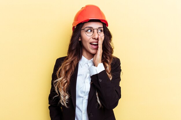 Young architect mixed race woman isolated on yellow background is saying a secret hot braking news and looking aside