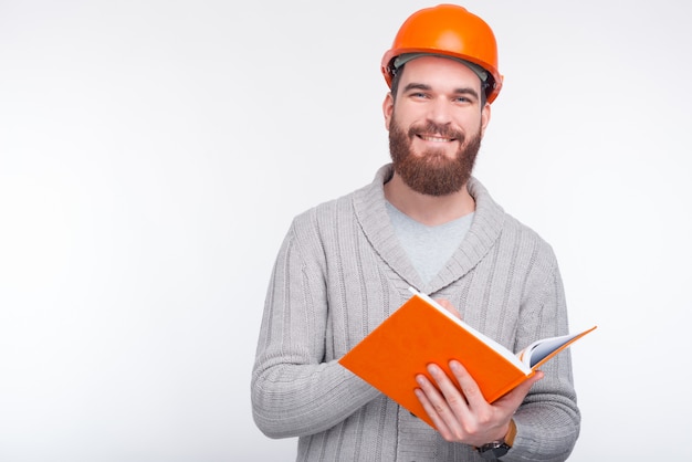 Young architect wearing hard hat is writing something in an orange book.