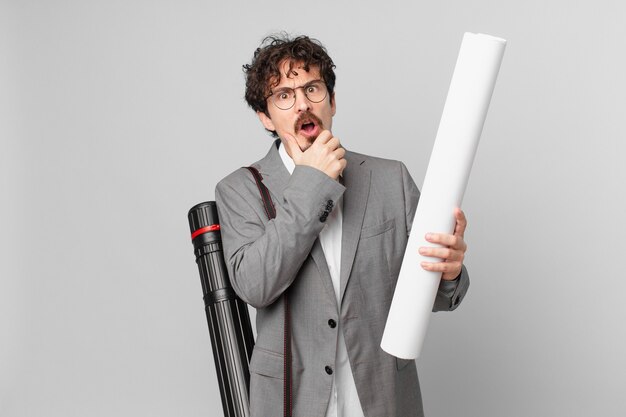 Young architect with mouth and eyes wide open and hand on chin