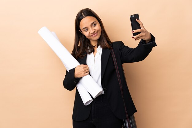 Giovane donna dell'architetto che tiene i modelli sopra la parete isolata che fa un selfie