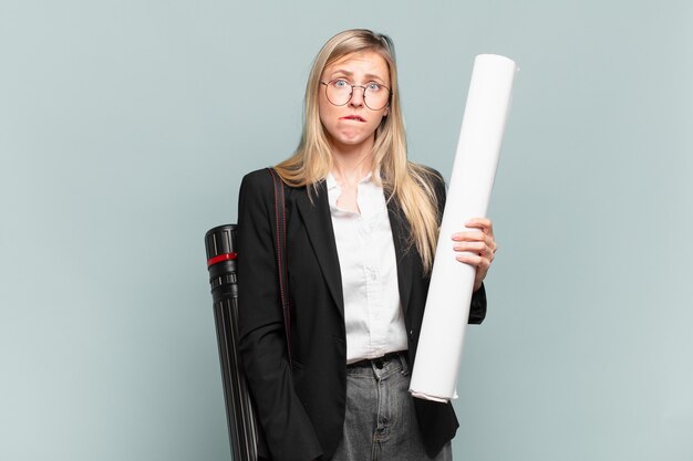 Young architect woman looking puzzled and confused, biting lip with a nervous gesture, not knowing the answer to the problem