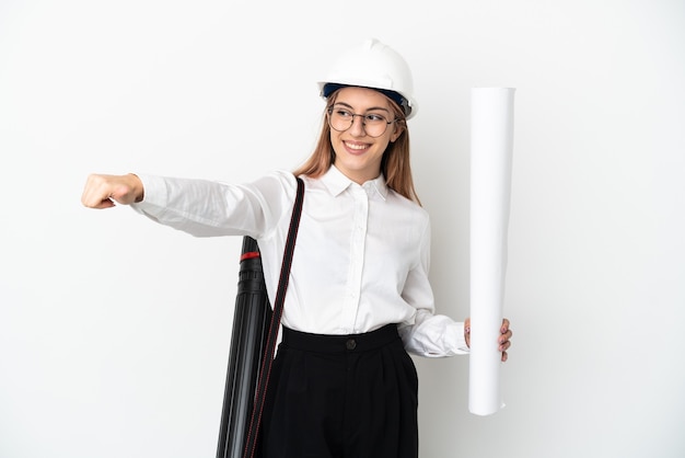 Young architect woman with helmet and holding blueprints isolated on white background giving a thumbs up gesture