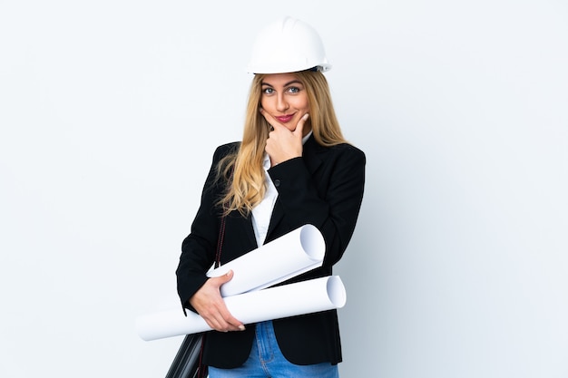 Giovane donna dell'architetto con il casco e che tiene i modelli sopra la risata bianca isolata