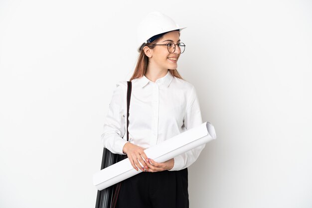 Young architect woman with helmet and holding blueprints isolated