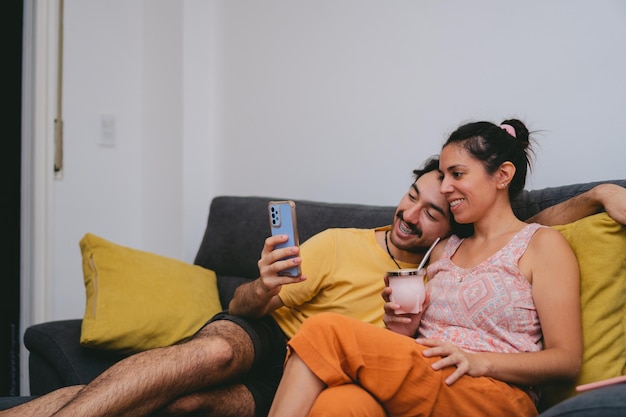 Young Argentine couple making a video call on their couch at home while drinking mate Copy space