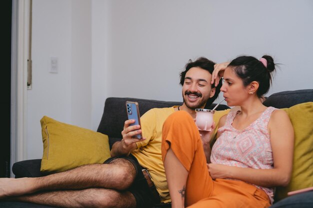 Young Argentine friends drinking mate while looking at their cell phone on the sofa at home Copy space