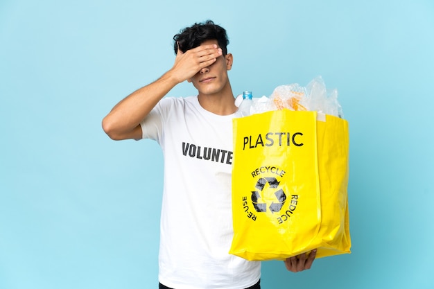 Young Argentinian man holding a bag full of plastic covering eyes by hands. Do not want to see something