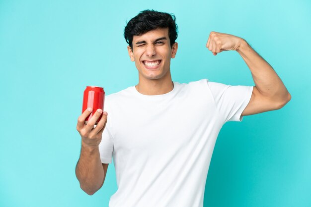 Young Argentinian man holding a refreshment isolated on blue background doing strong gesture