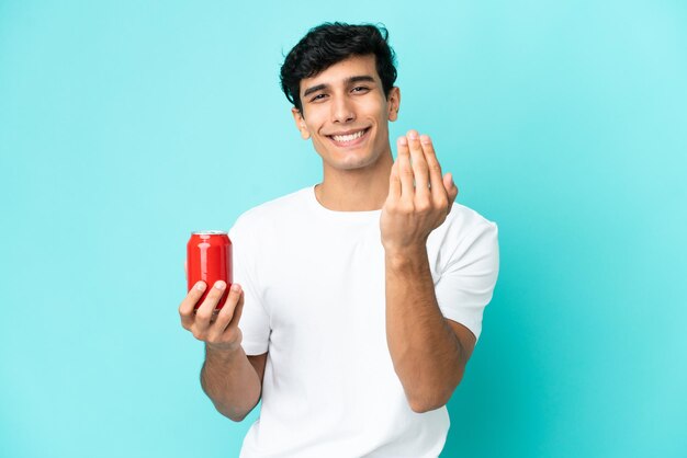 手で来るように誘う青い背景で隔離の軽食を保持している若いアルゼンチン人。あなたが来て幸せ