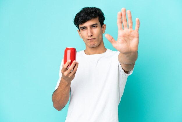 Young Argentinian man holding a refreshment isolated on blue background making stop gesture