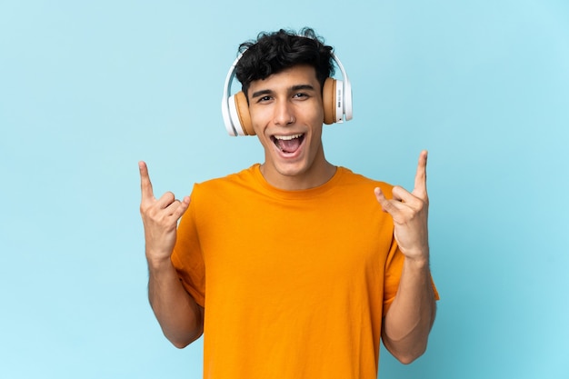 Young Argentinian man isolated on background listening music making rock gesture