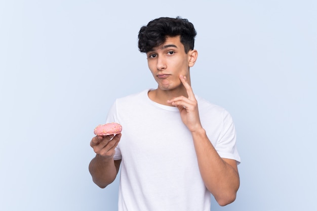 Young Argentinian man over isolated blue wall holding a donut